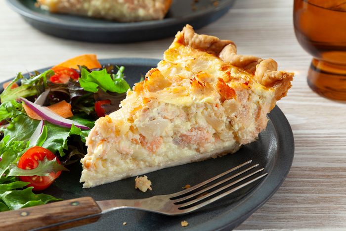 A slice of salmon pie on a plate with a salad.