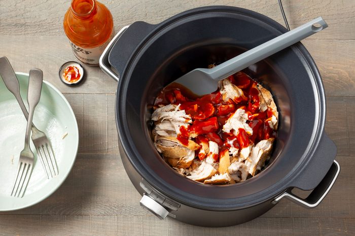 Chicken with Barbecue Sauce over it in a slow cooker on wooden surface