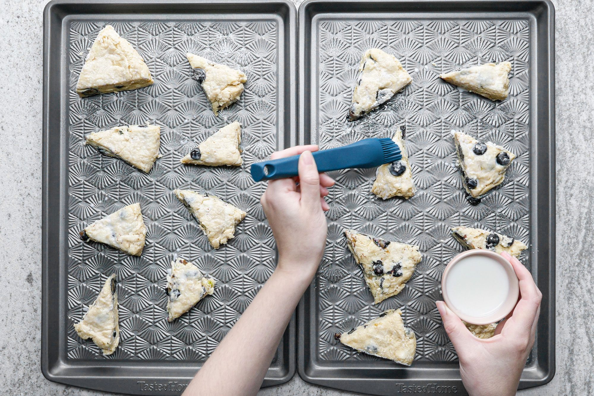Brushing Milk on Raw Blueberry Scones Placed on Baking Trays on Marble Surface