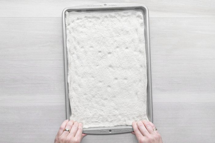 Pizza crust unrolled on a baking pan on a wooden surface