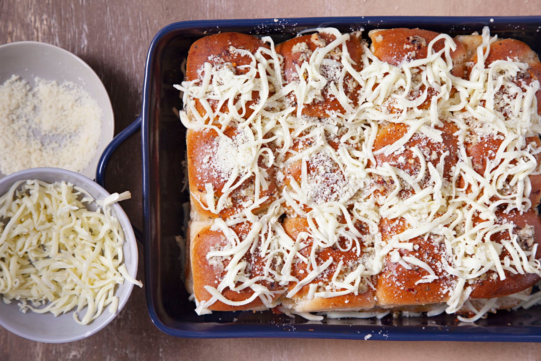 Sprinkled cheese on sliders on a baking tray