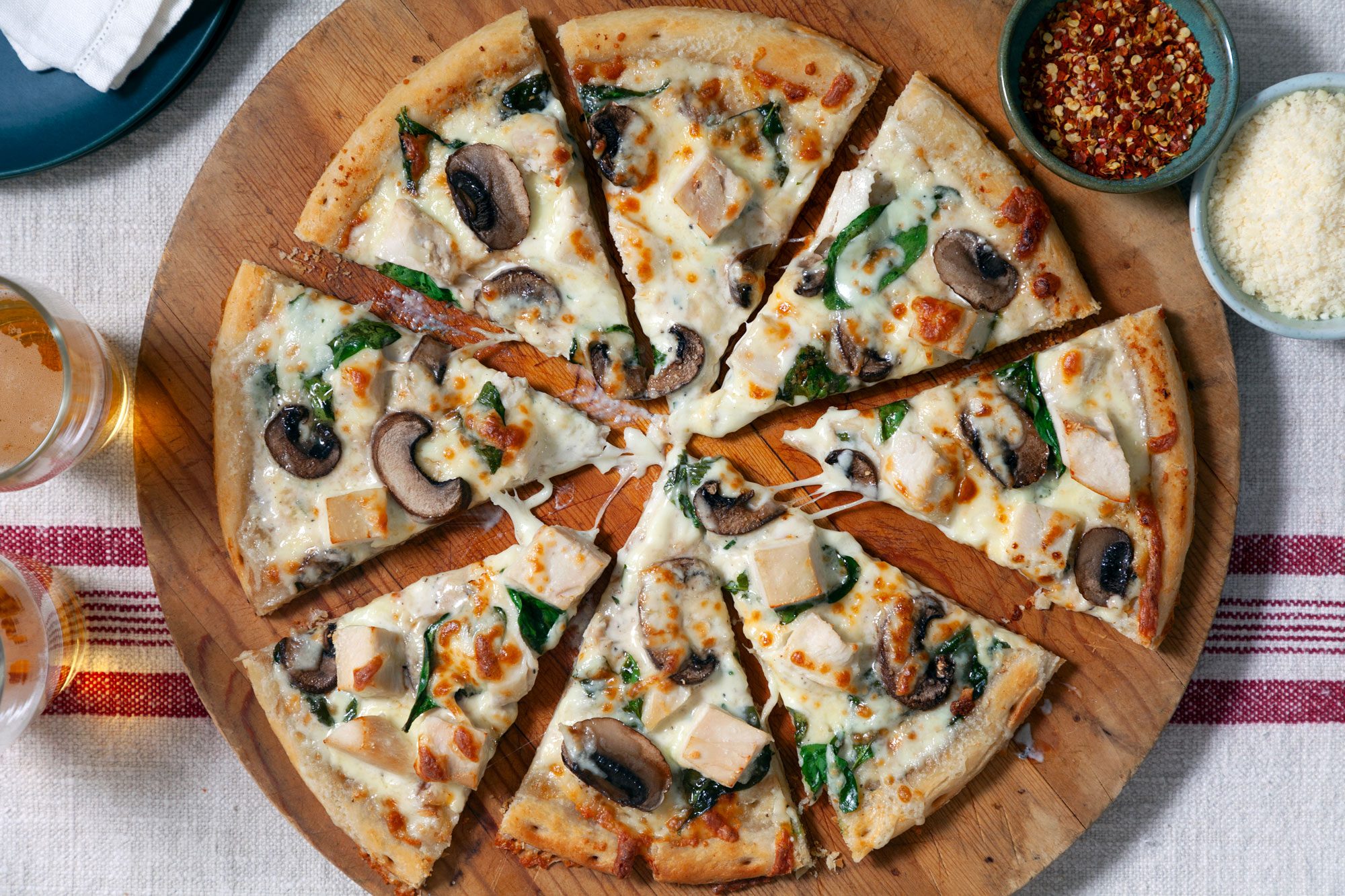 Chicken Alfredo Pizza sliced and ready to eat with beer glasses on the side