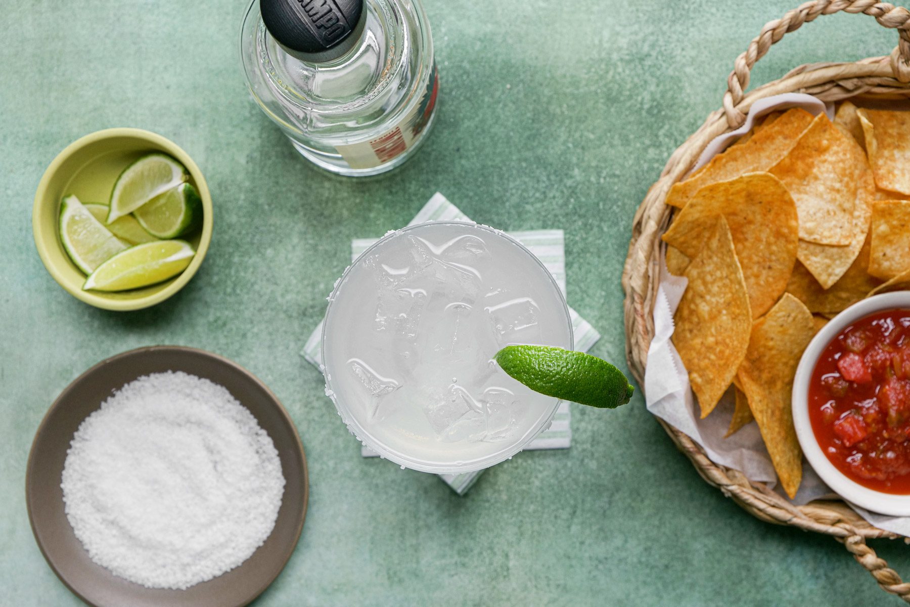 A glass of classic margarita with lime wedges and chips
