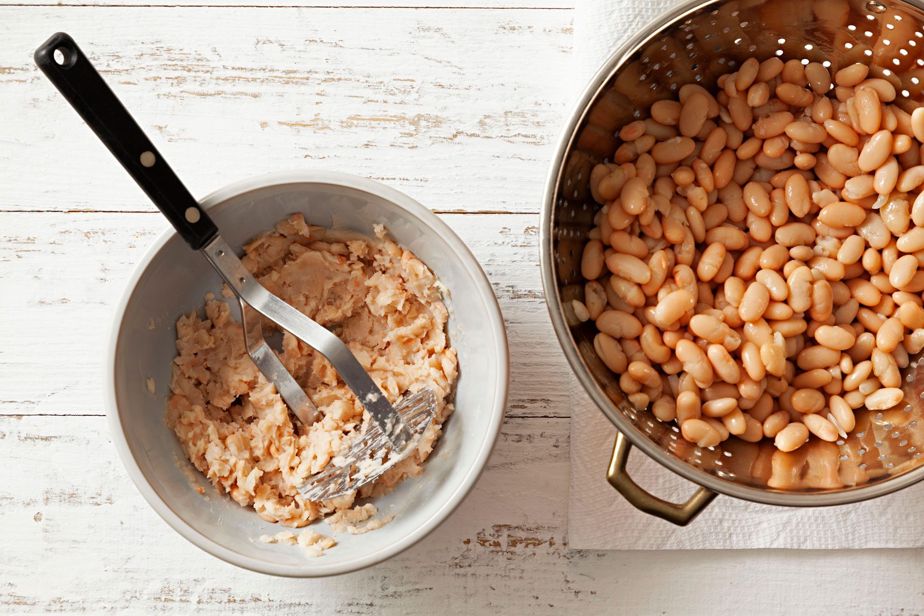 Mashed beans in a small bowl with a potato masher