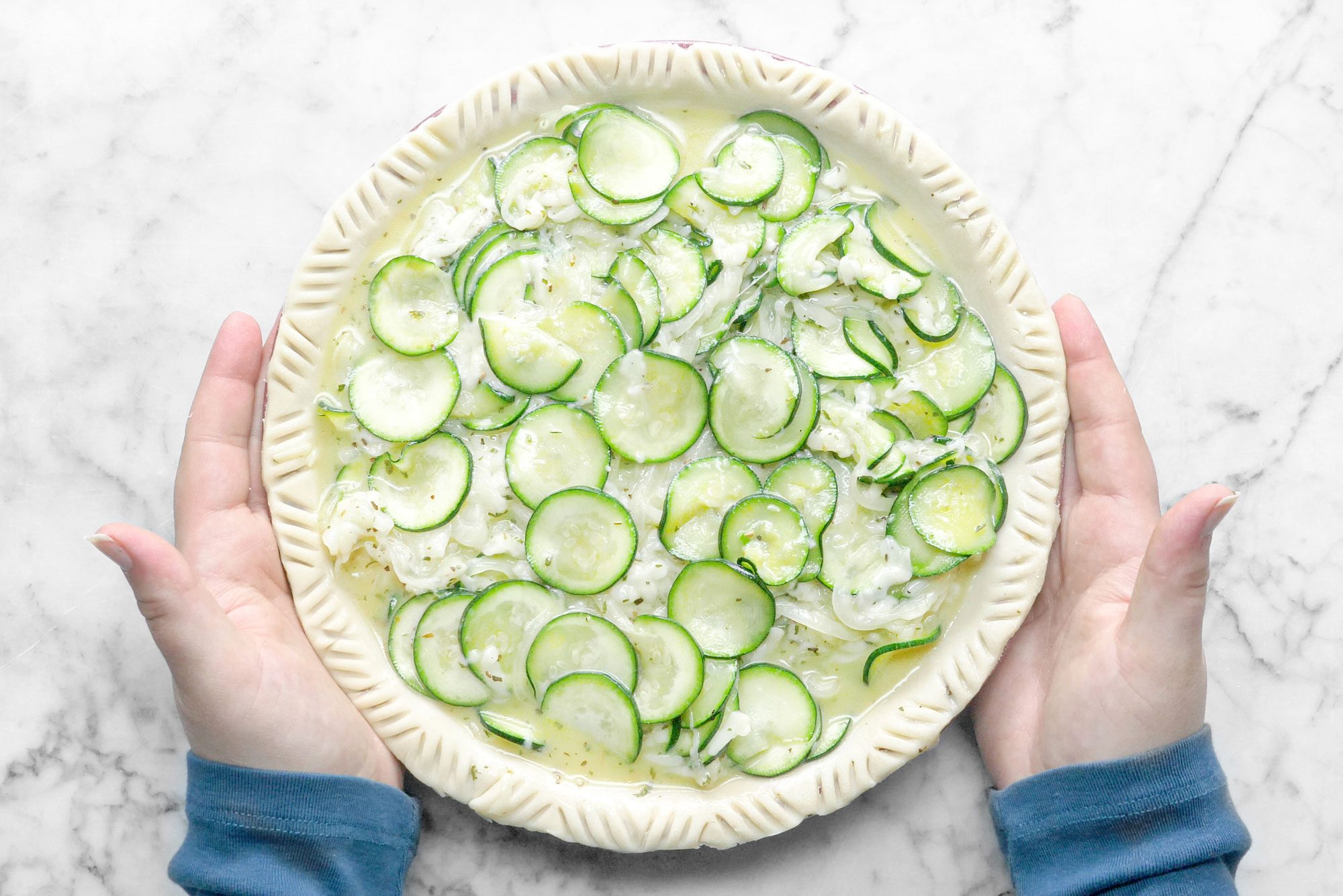 Zucchini Quiche In a Pie Plate Held in Hands, Marble Background.
