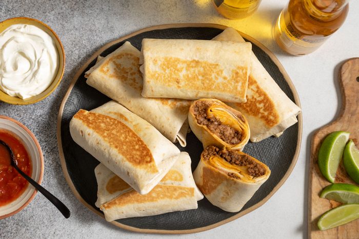 Burritos served in an oval shaped plate with a bowl of sour cream