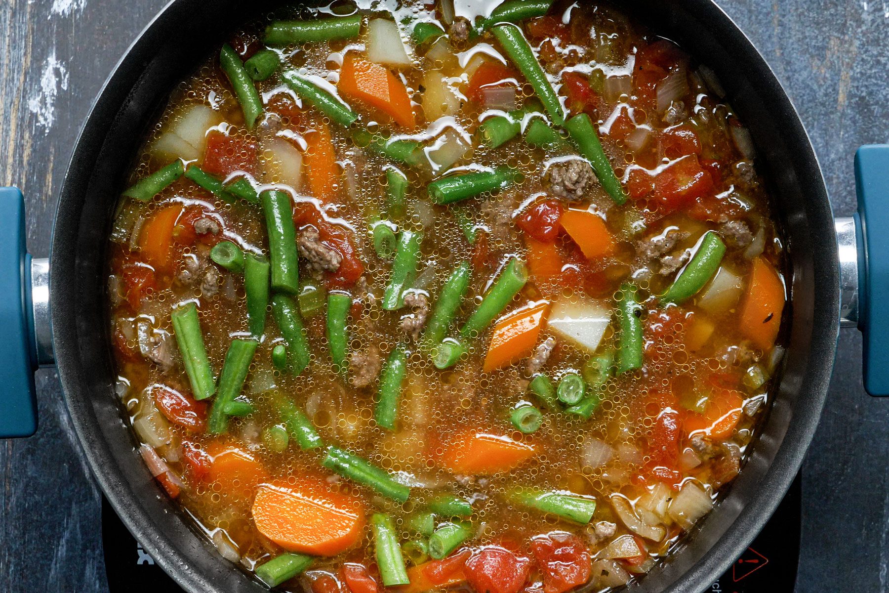 Hamburger Soup cooking in a large saucepan, placed on a wooden table.