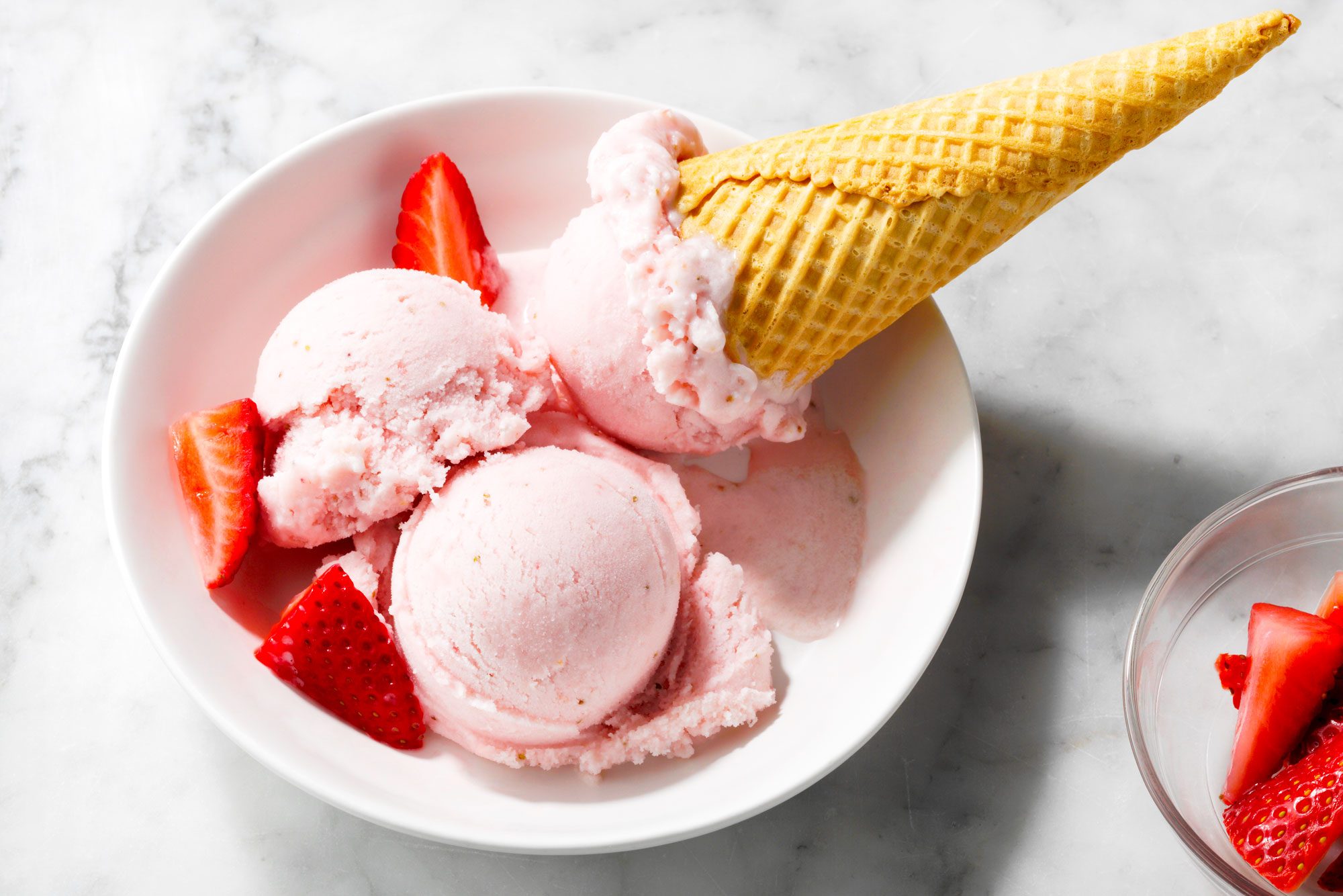 wide shot of strawberry gelato in a bowl; cones; marble surface;