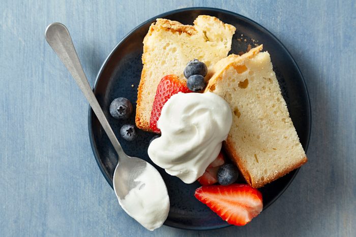 Bread and Berries Topped with Sweetened Whipped Cream Served on a black small plate placed on a textured light blue surface