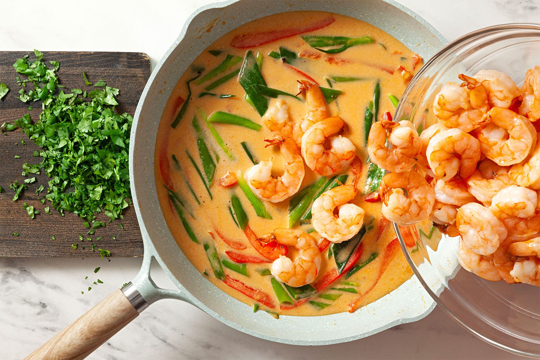 Adding shrimps to curry in skillet