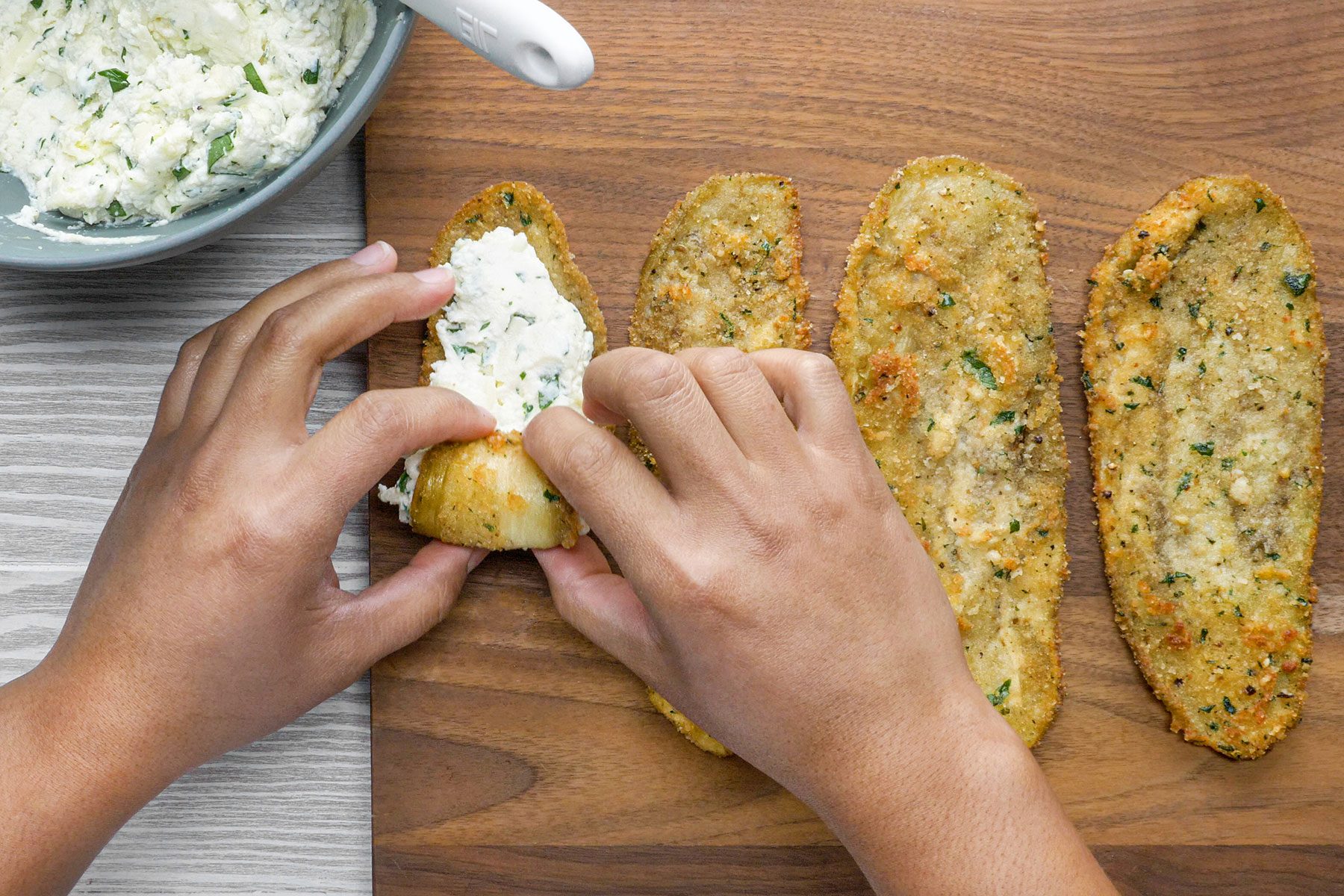Spreading cheese filling on fried eggplant slices on wooden base