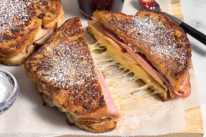Monte Cristo Sandwich served on wooden board with jar of jam on the side