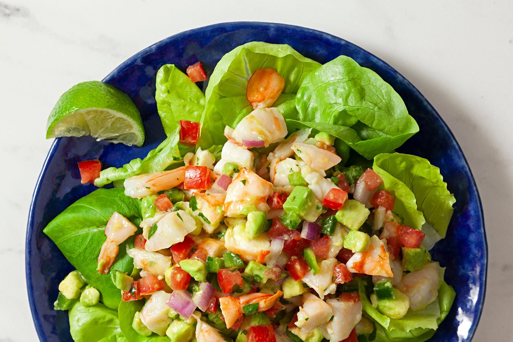 Top view shot of Shrimp Avocado Salad; served in lettuce leaves; blue plate; served with lime wedges; marble background;