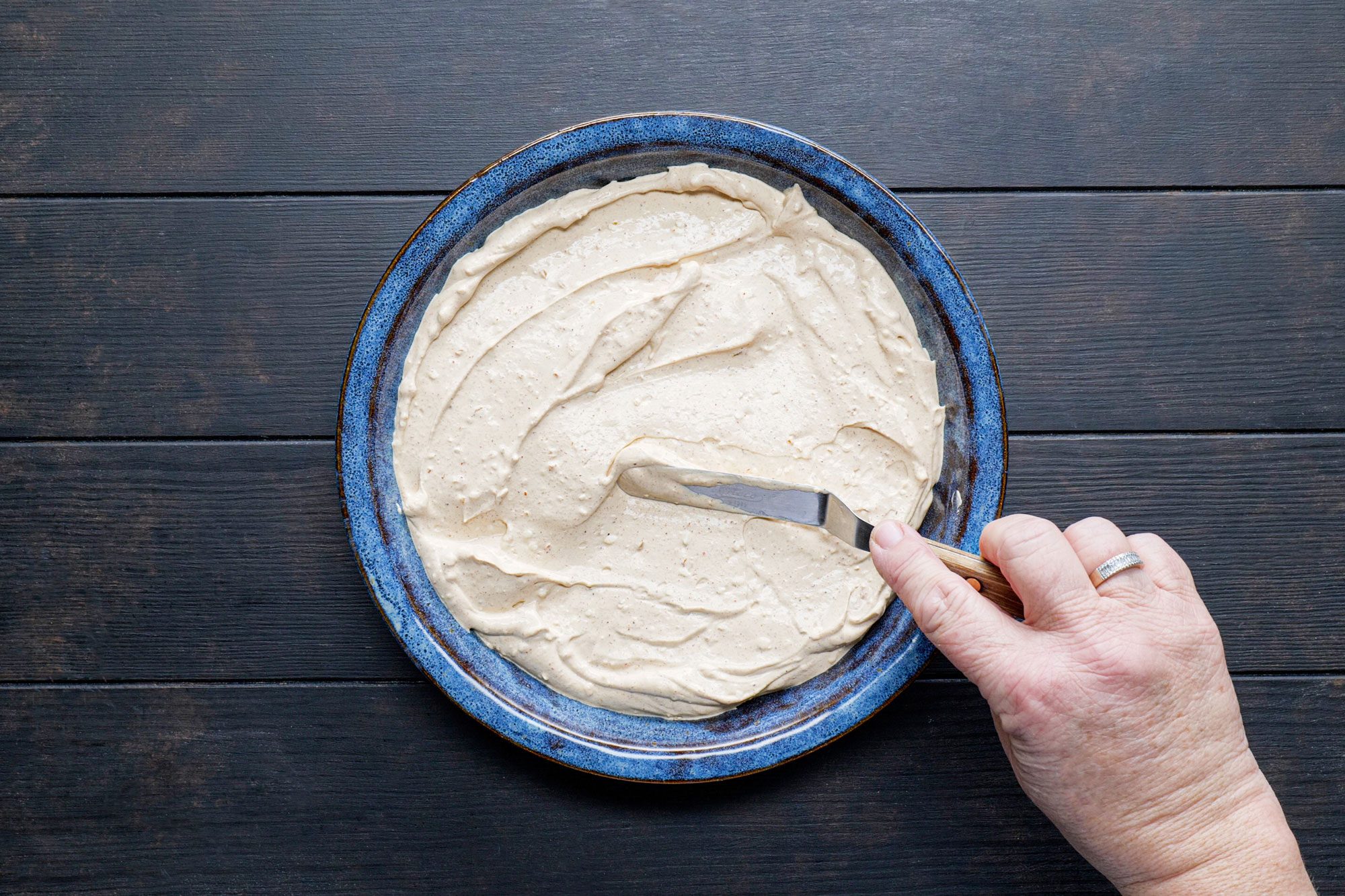 Spreading Taco Dip Cream on a pie plate on wooden surface