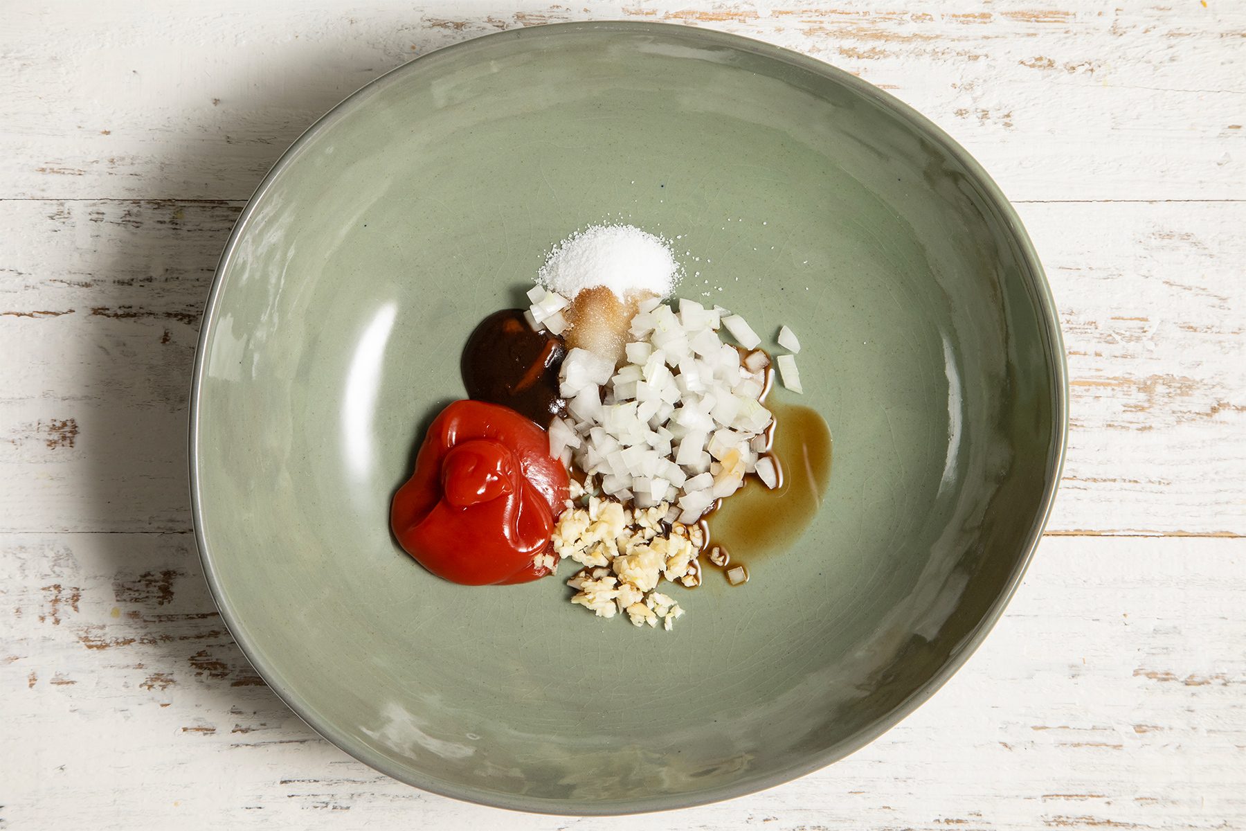 A green bowl on a white wooden surface contains various ingredients