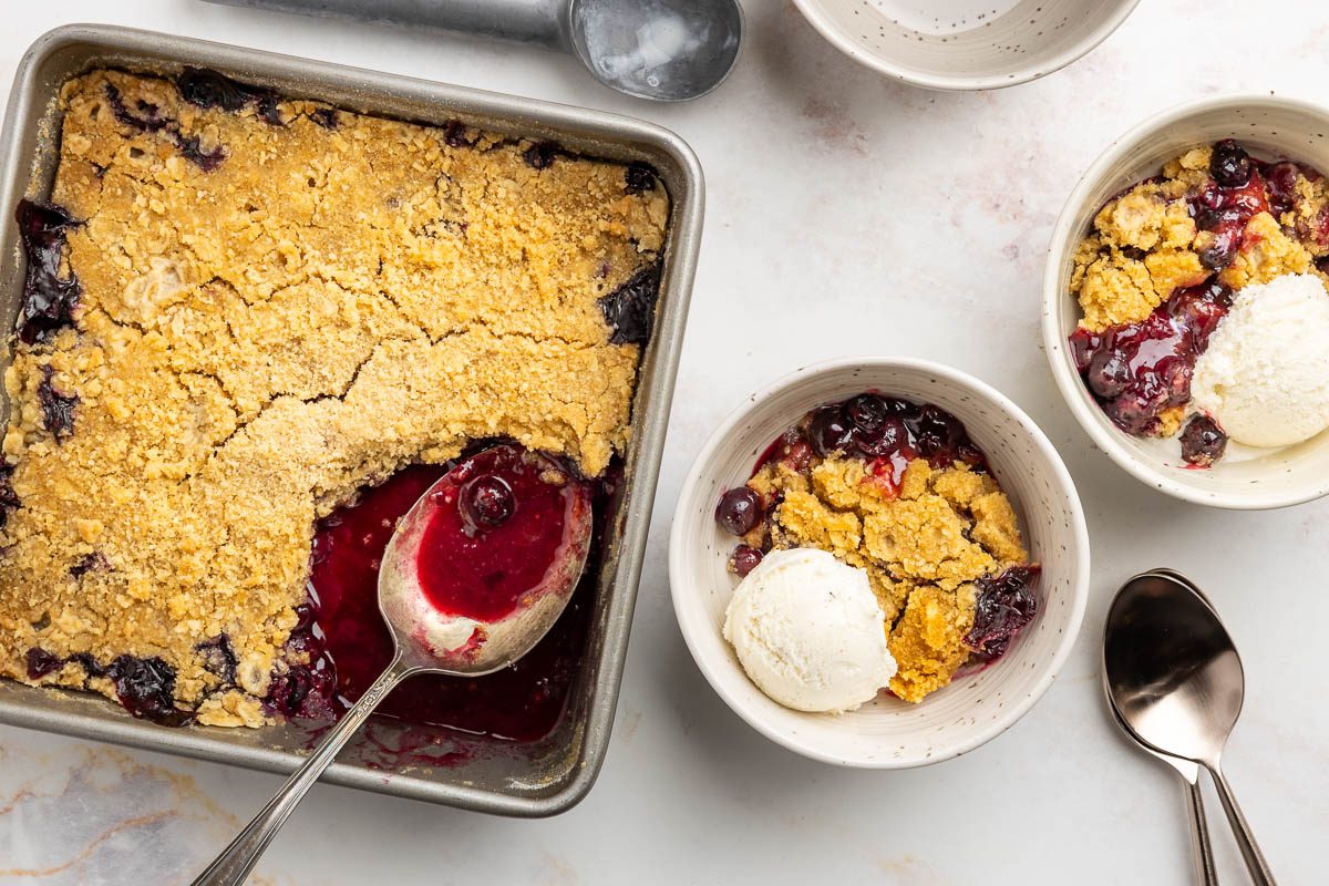 Taste of Home blueberry crisp recipe photo of blueberry crisp in baking dish, 2 bowls with dessert topped with vanilla ice cream.