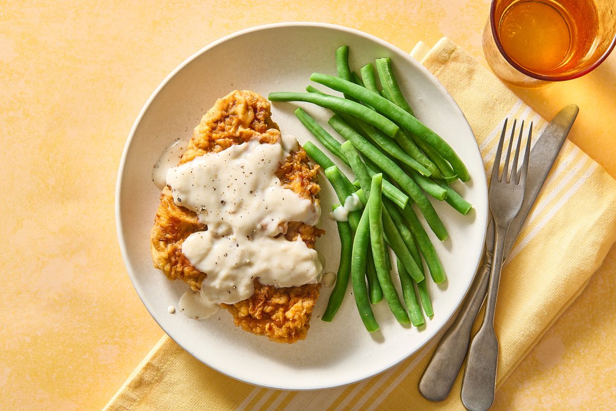 Overhead shot of chicken fried steak and gravy on a plate with some green beans