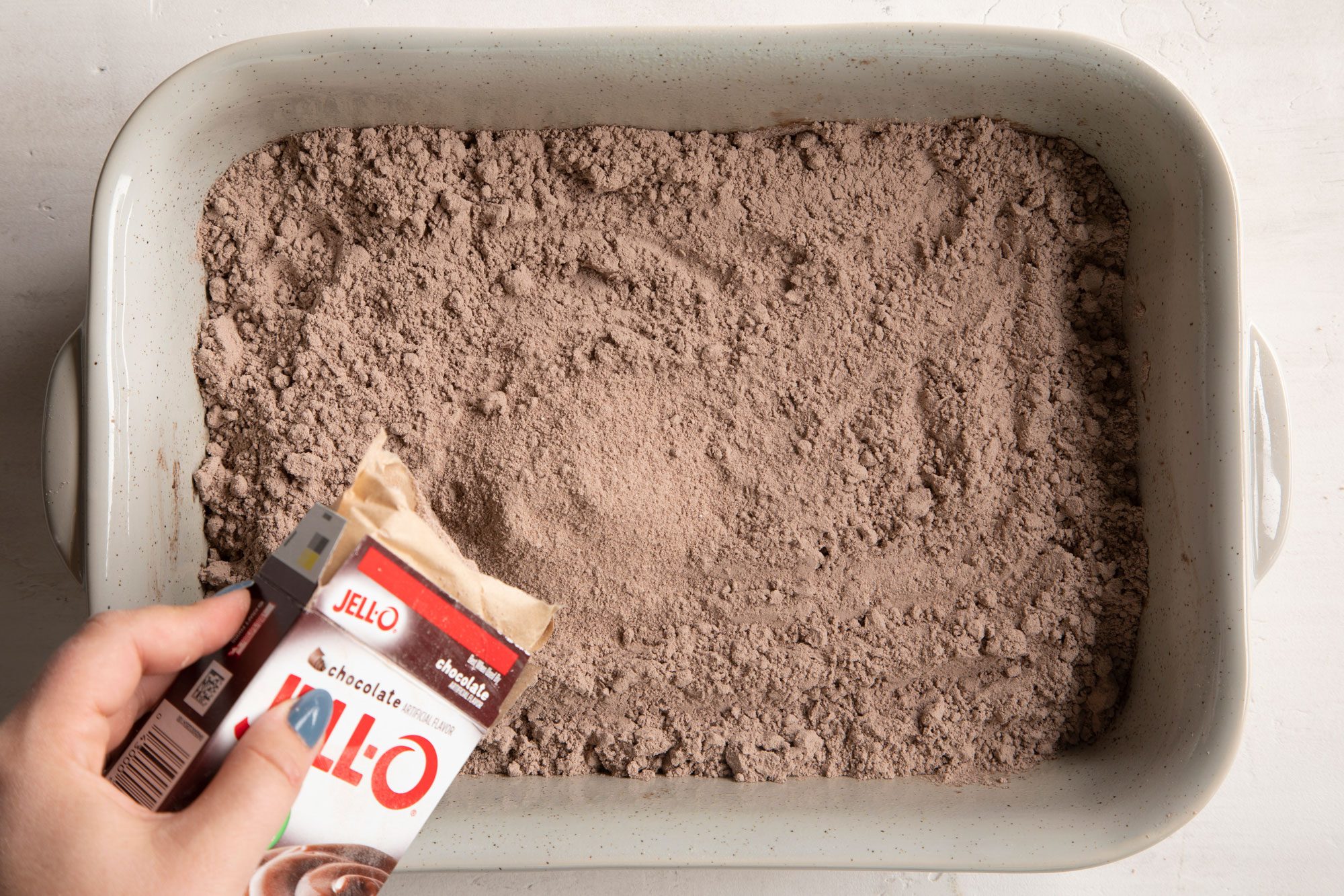 pouring dry pudding mix on dry cake mix in a rectangular baking dish