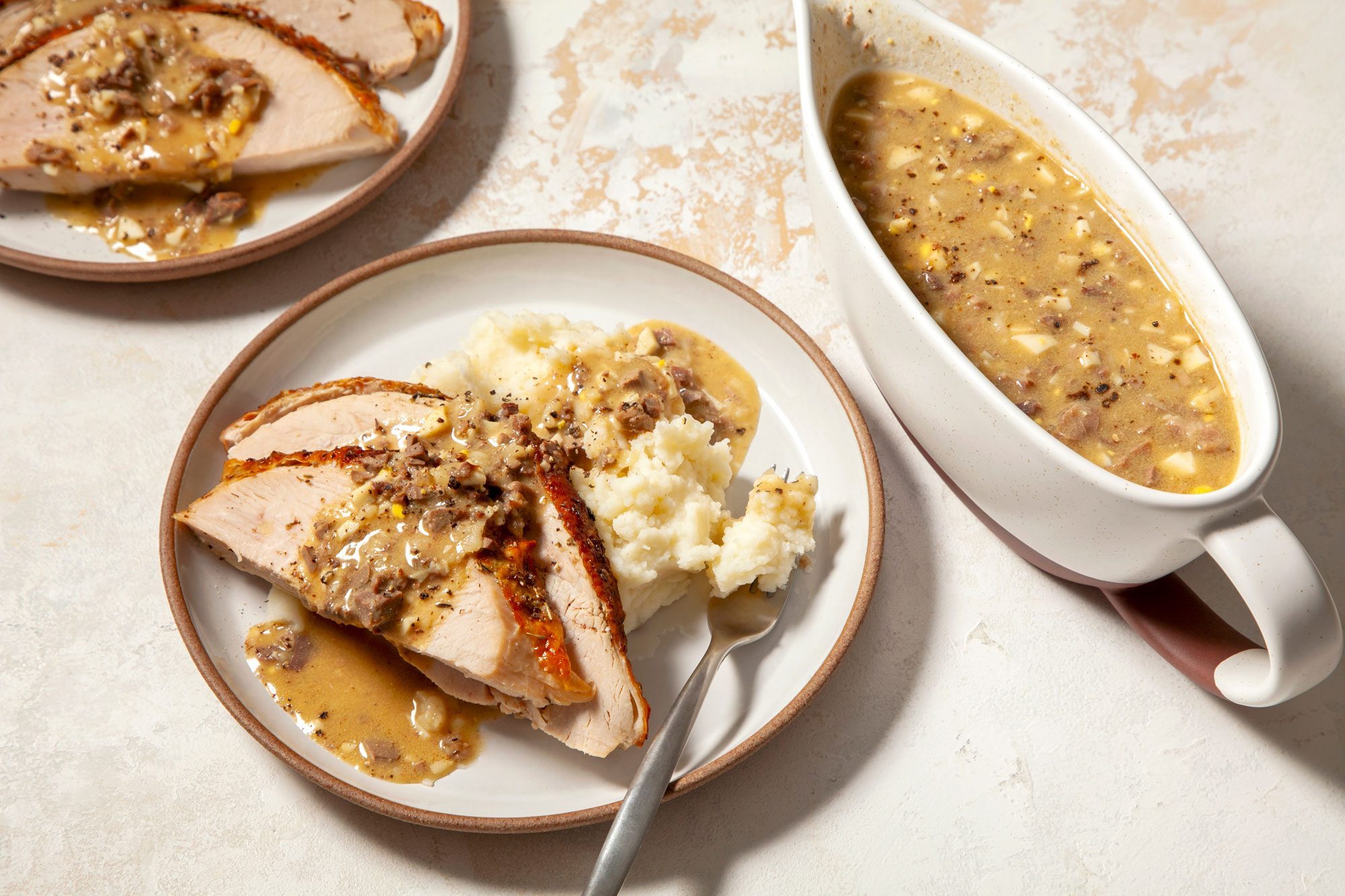 Turkey Giblet Gravy served in a fancy bowl with gravy poured over slices of roast turkey breasts and mashed potatoes