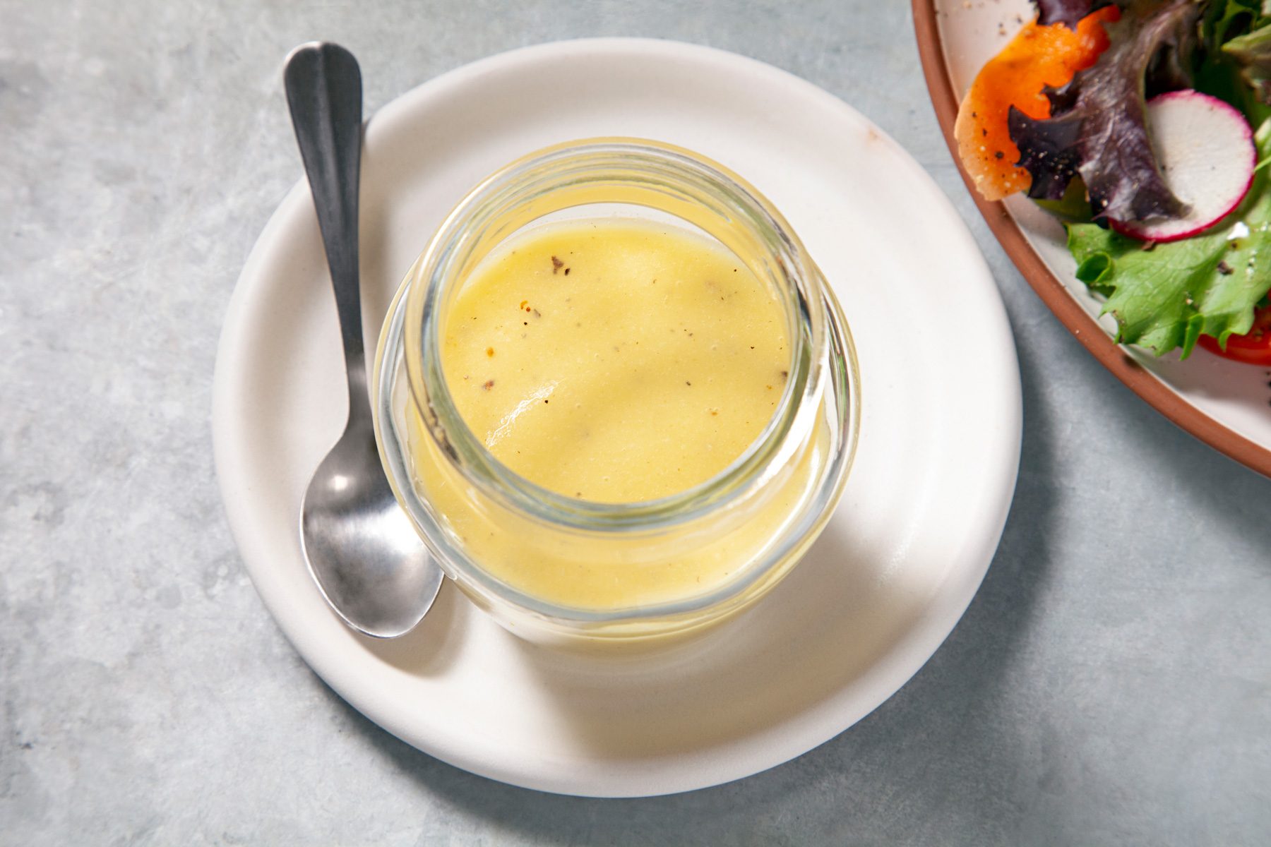 A jar of Lemon Vinaigrette dressing on a plate with a spoon
