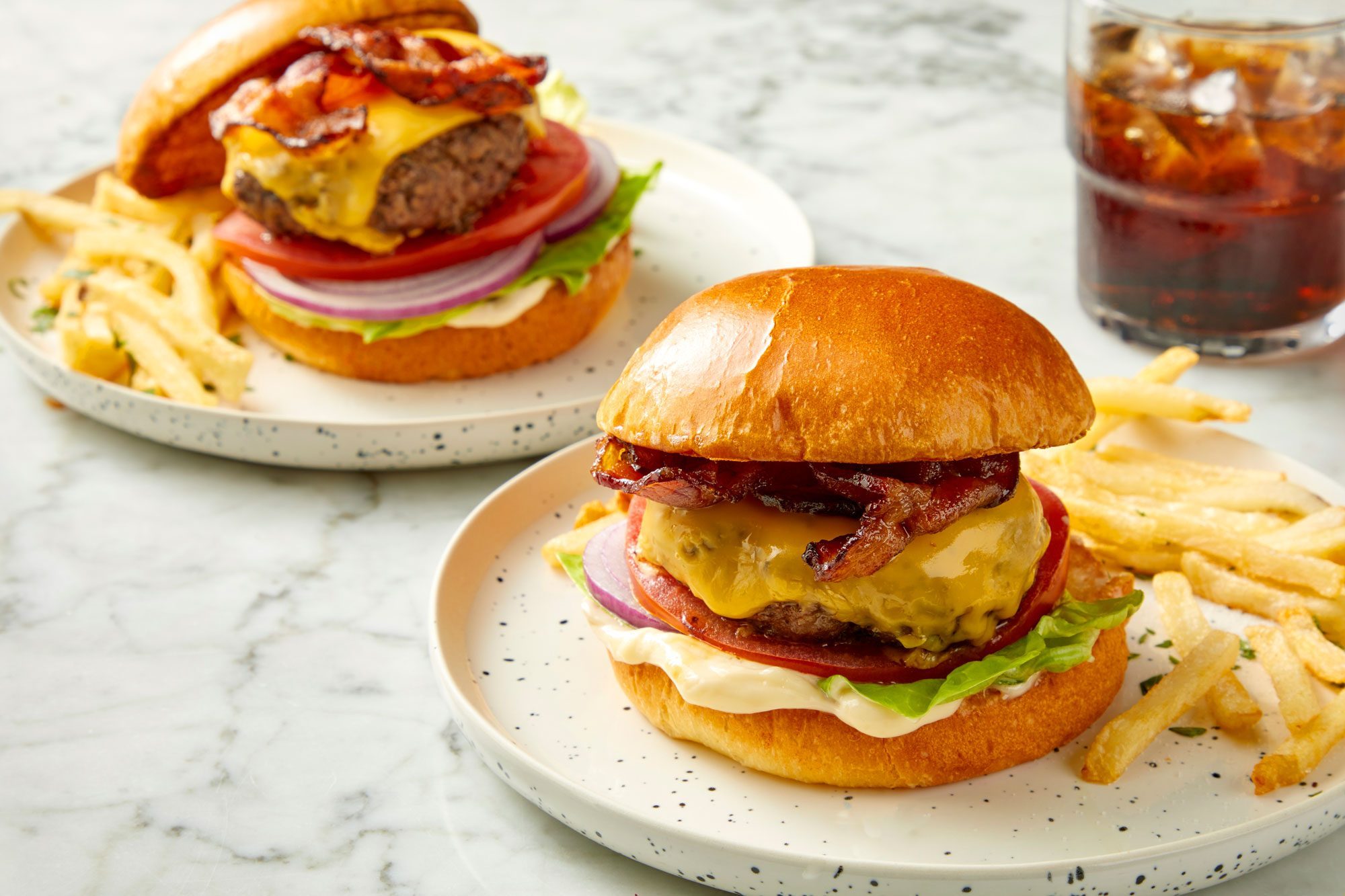 3/4 angle view shot of Easy Oven-Baked Burgers; served on plates with fries; drink; marble background;