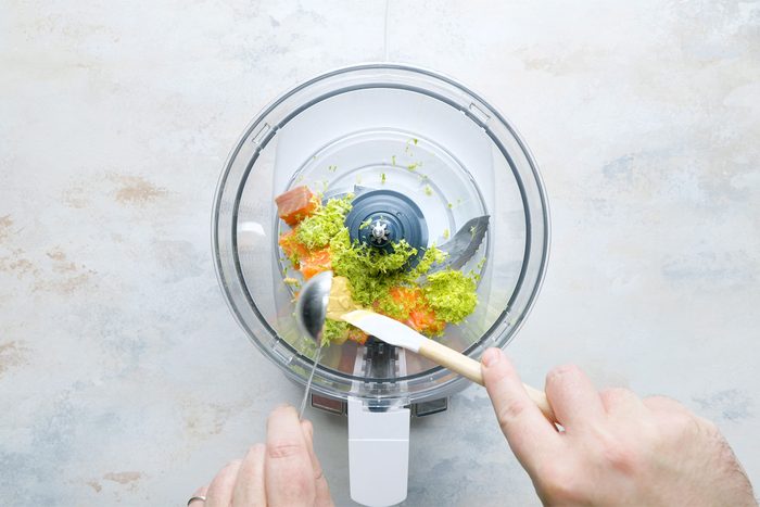 Overhead shot of place a fourth of the salmon in a food processor; add lime zest and mustard; process until smooth; spoon; spatula; white marble background;