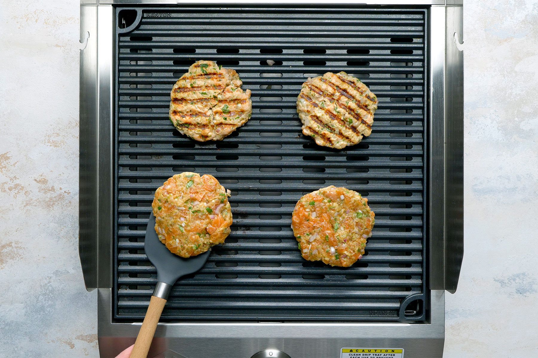 Overhead shot of griller; grill patties overv medium heat; heat 4-5 mintues on each sides; flat spatual; white marble background;