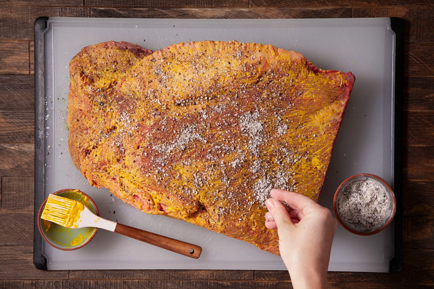 A person rubbing salt and pepper mixture over the brisket