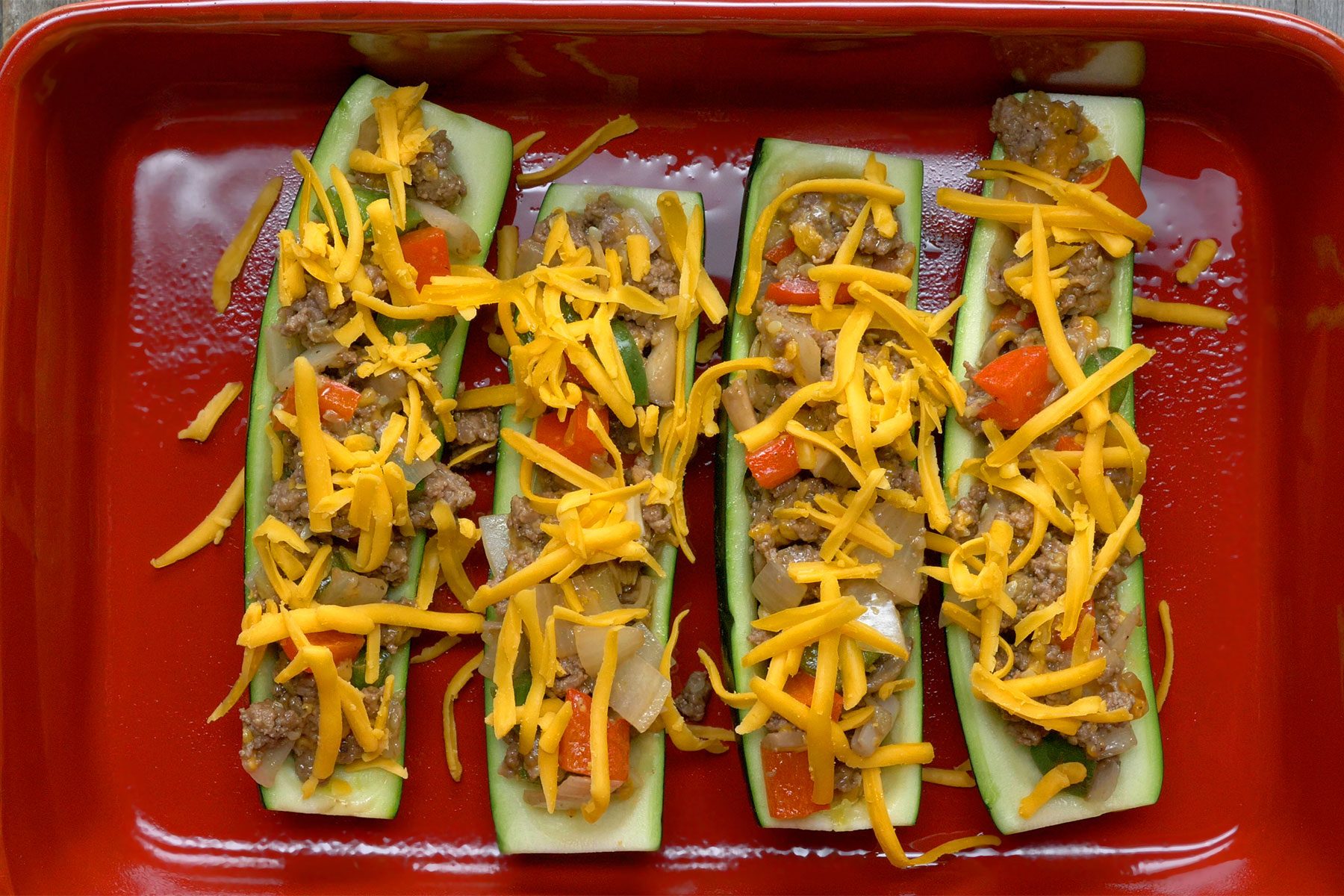 Overhead shot of sprinkled with remaining cheese; red baking dish; wooden background;