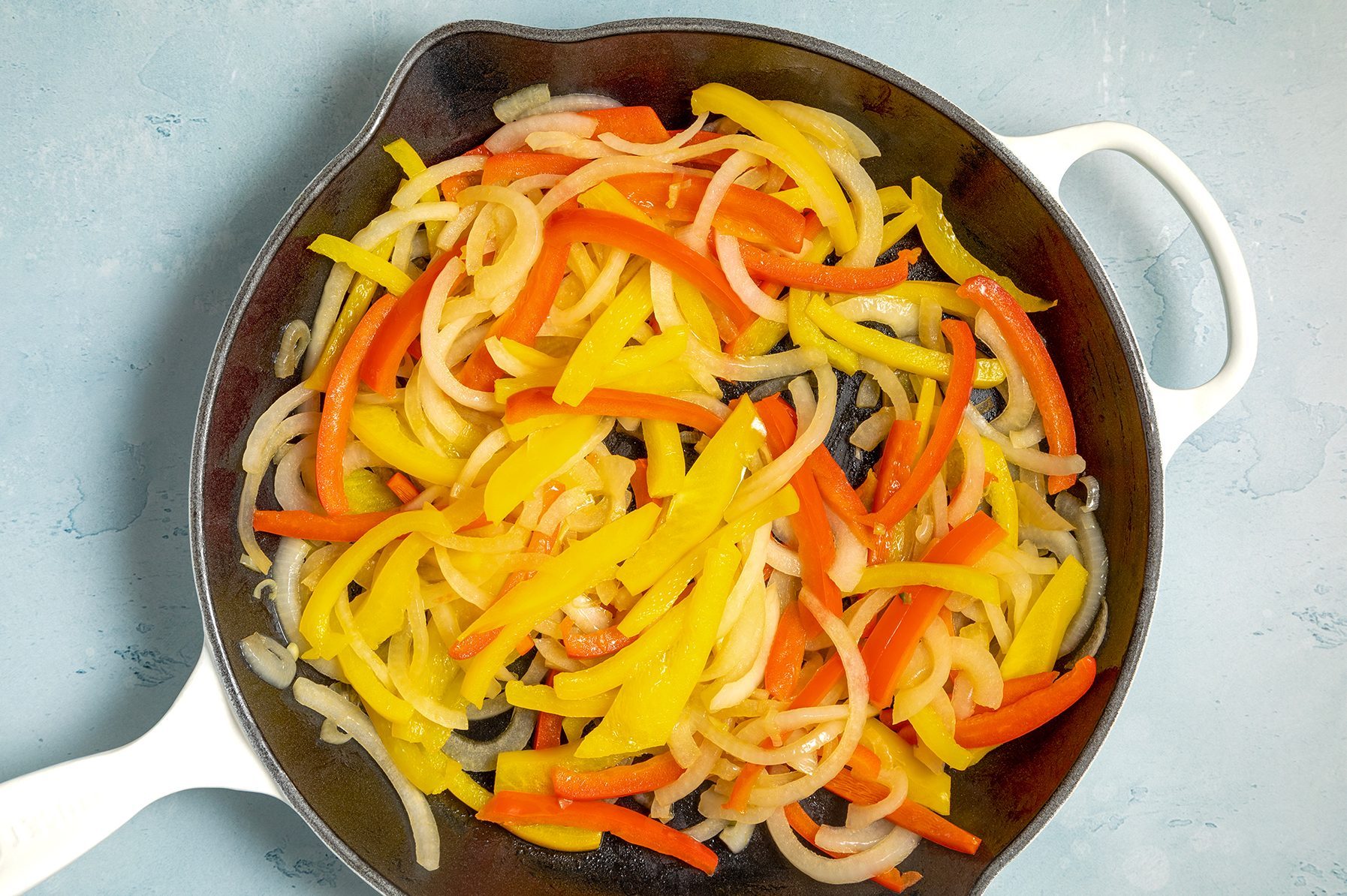 A skillet filled with sautéed bell peppers and onions, featuring a mix of yellow, orange, and red pepper strips, along with thinly sliced onion, all lightly browned and cooked.