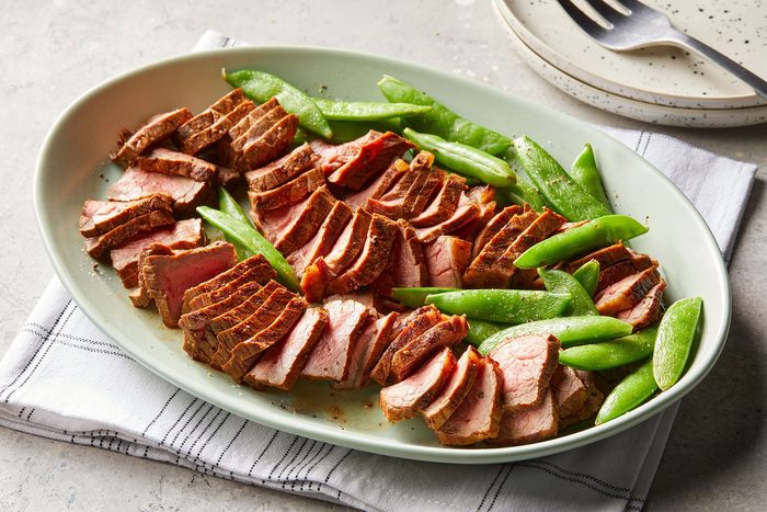 3/4 angle view shot of Grilled Short Ribs; served on large platter with beans; small plates; fork; napkin; marble background