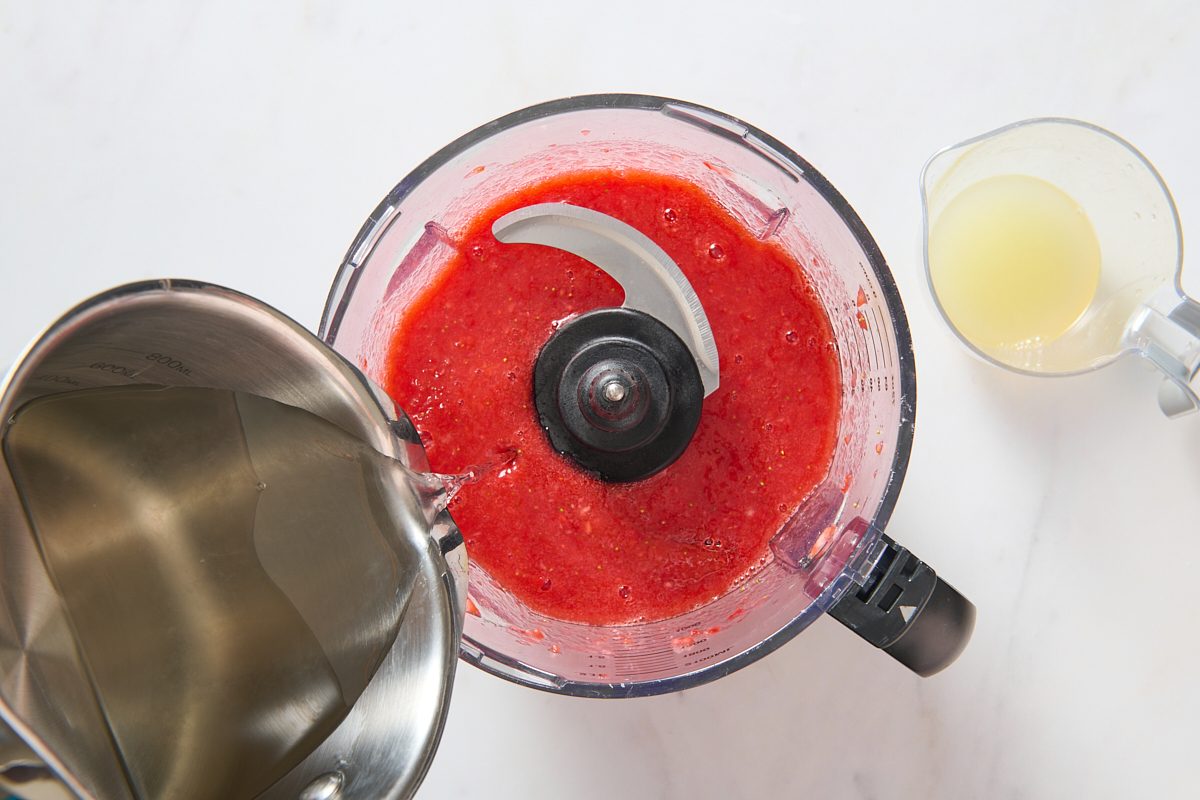 Sugar syrup being added to strawberry mixture in food processor