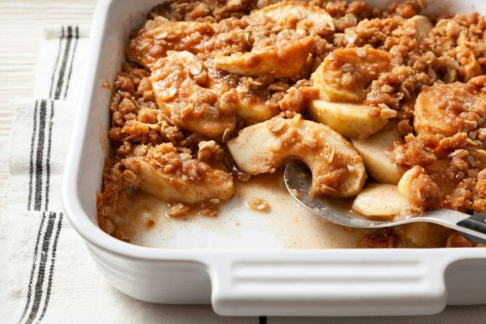 close shot; wooden background; Vegan Apple Crisp in a square baking dish over kitchen towel;