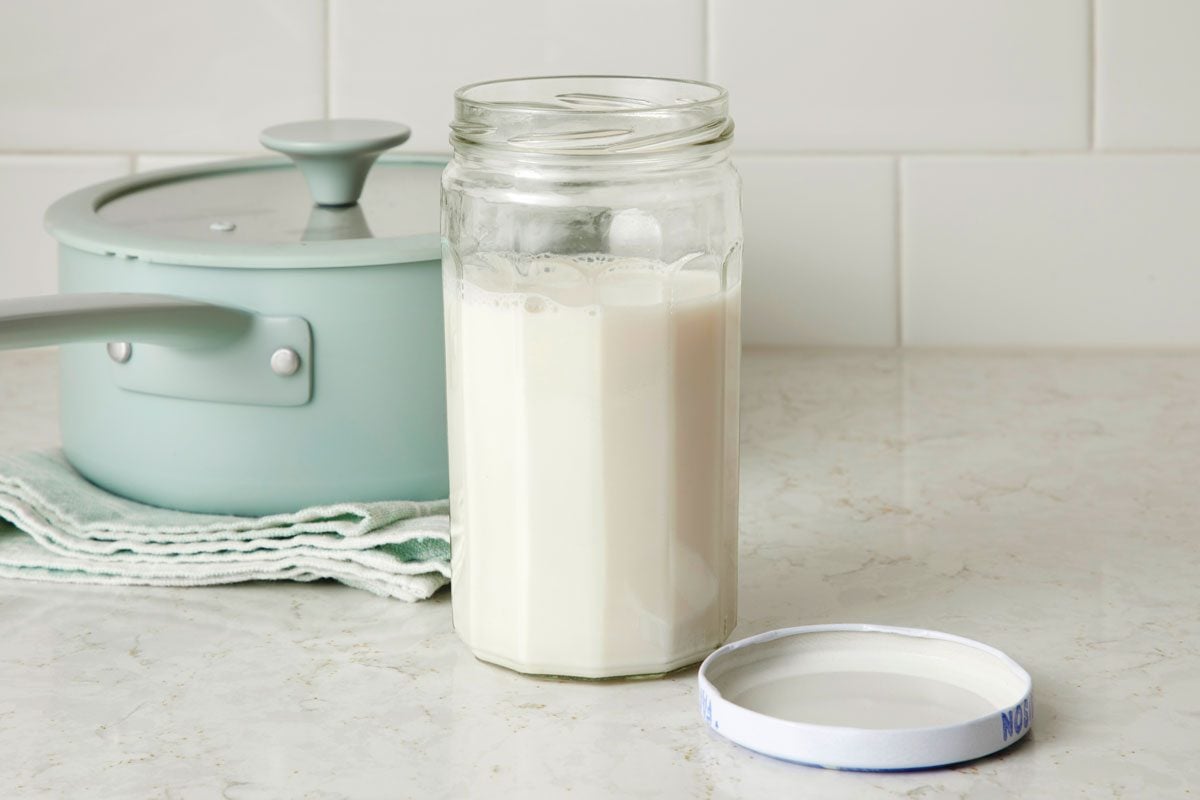 Nut milk in a glass jar on a kitchen counter with saucepan in the background nearby