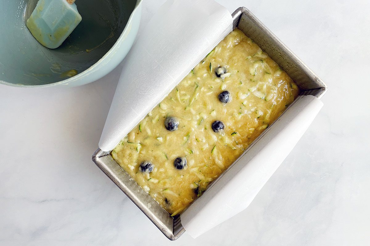 Step three in making Taste of Home's Blueberry Zucchini Bread involves pouring the batter into a lined loaf pan