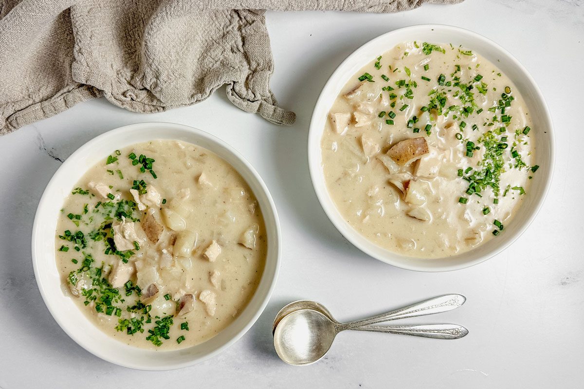 Taste of Home chicken potato soup in white ceramic bowls with a linen napkin on a marble surface.