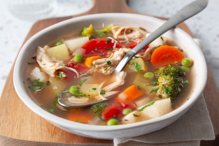 Single serving of Taste of Home Chicken Vegetable Soup in a white bowl on a wooden cutting board and a beige linen with a spoon