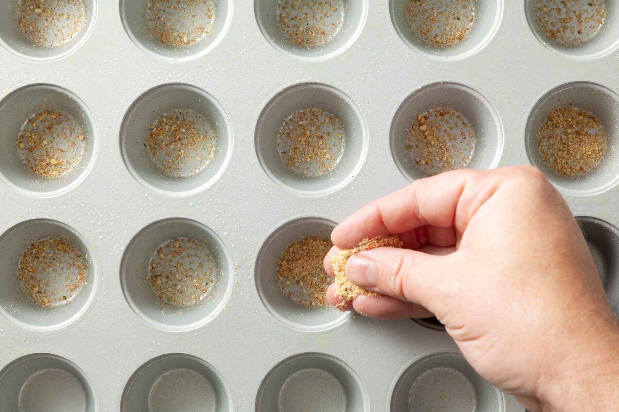Overhead shot of sprinkle 1/4 cup bread crumbs into 36 greased mini-muffin cups;