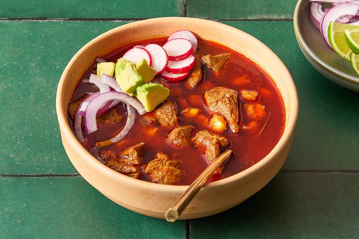 Closeup of a bowl of posole topped with red onion, avocado and radish