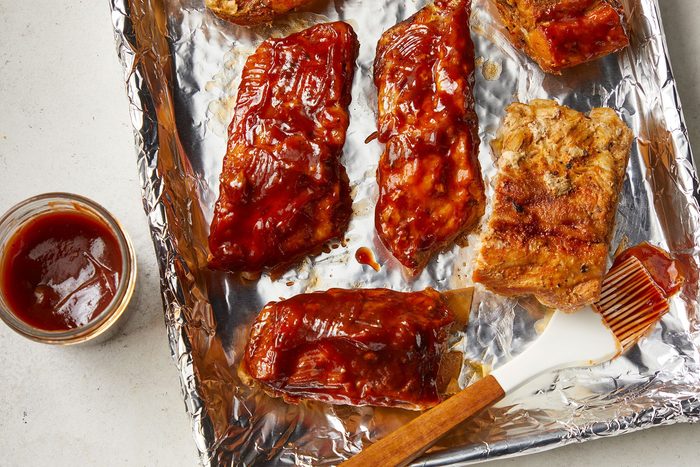 Overhead shot of transfer ribs to foil-lined baking pan; brush with sauce; marble background