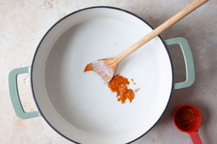 Coconut milk in a Dutch oven with red curry paste being added
