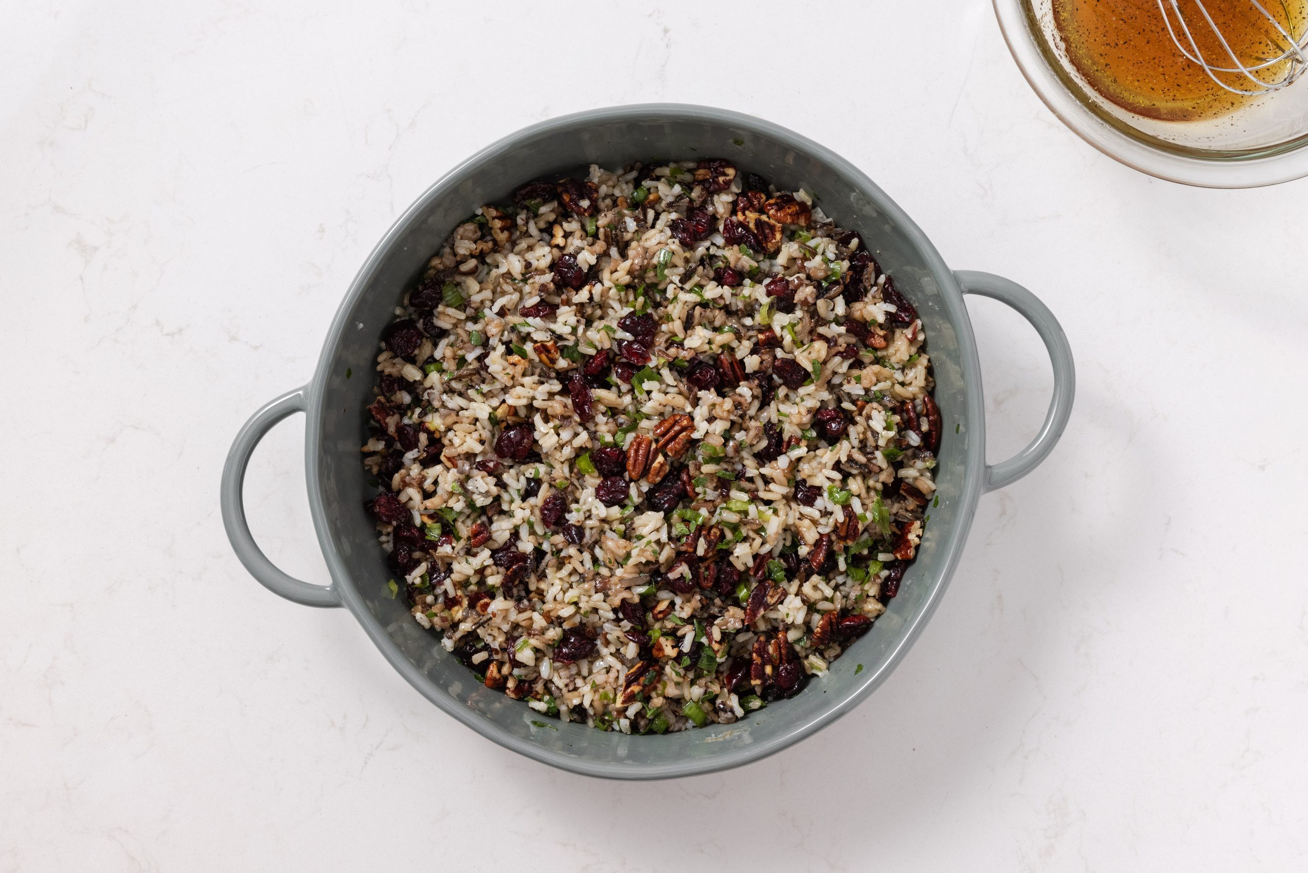 Wild rice salad in serving bowl being tossed with dressing.