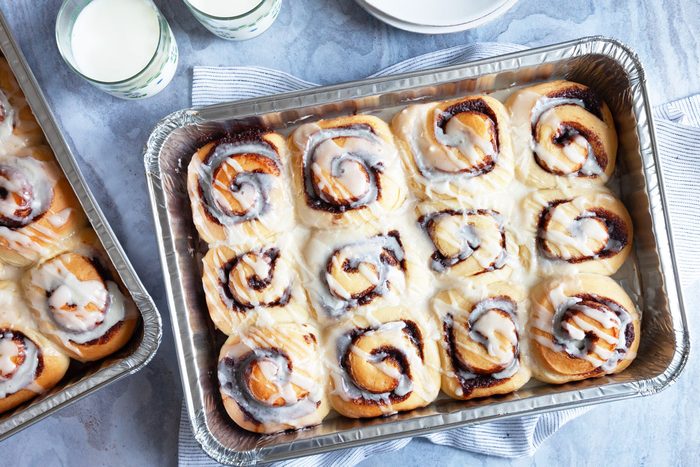 Full yield of Taste of Home Amish Cinnamon Rolls in 13x9 pans with glasses of milk and stack of white plates