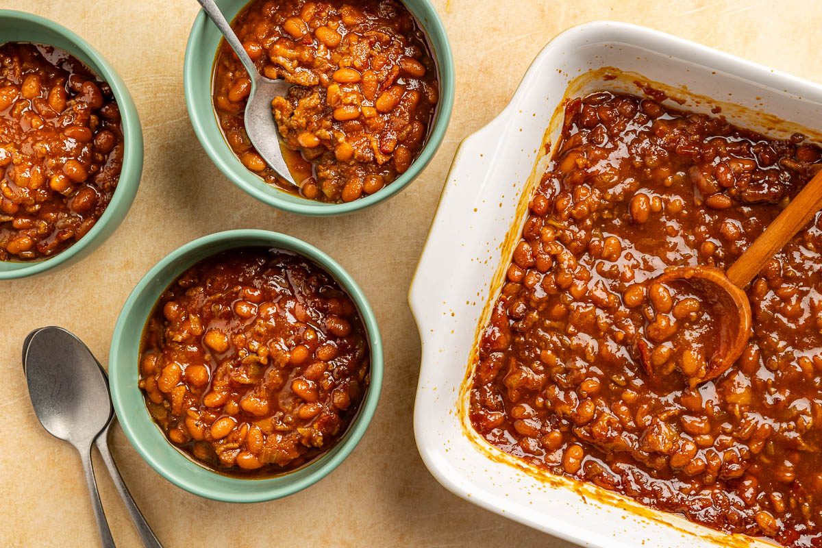 Taste of Home BBQ baked beans recipe photo of the beans finished into three bowls with baking dish popping in frame.