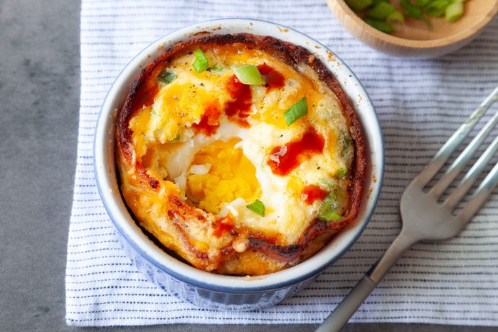 Taste of Home Bacon and Egg Muffins in blue ramekins, topped with green onions cheese, wooden bowl of green onions, forks