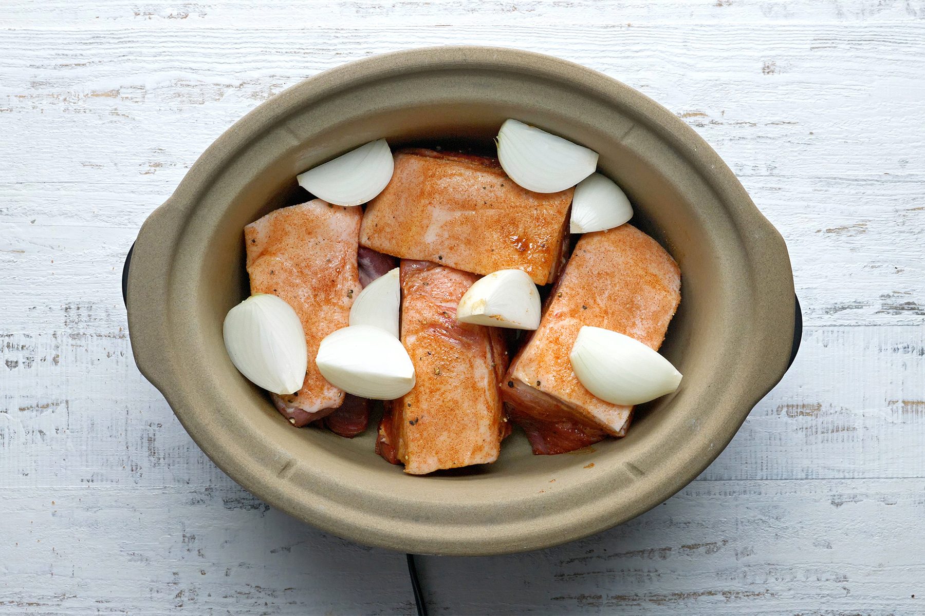 overhead shot; white textured background; Placed meat and onions in a slow cooker;