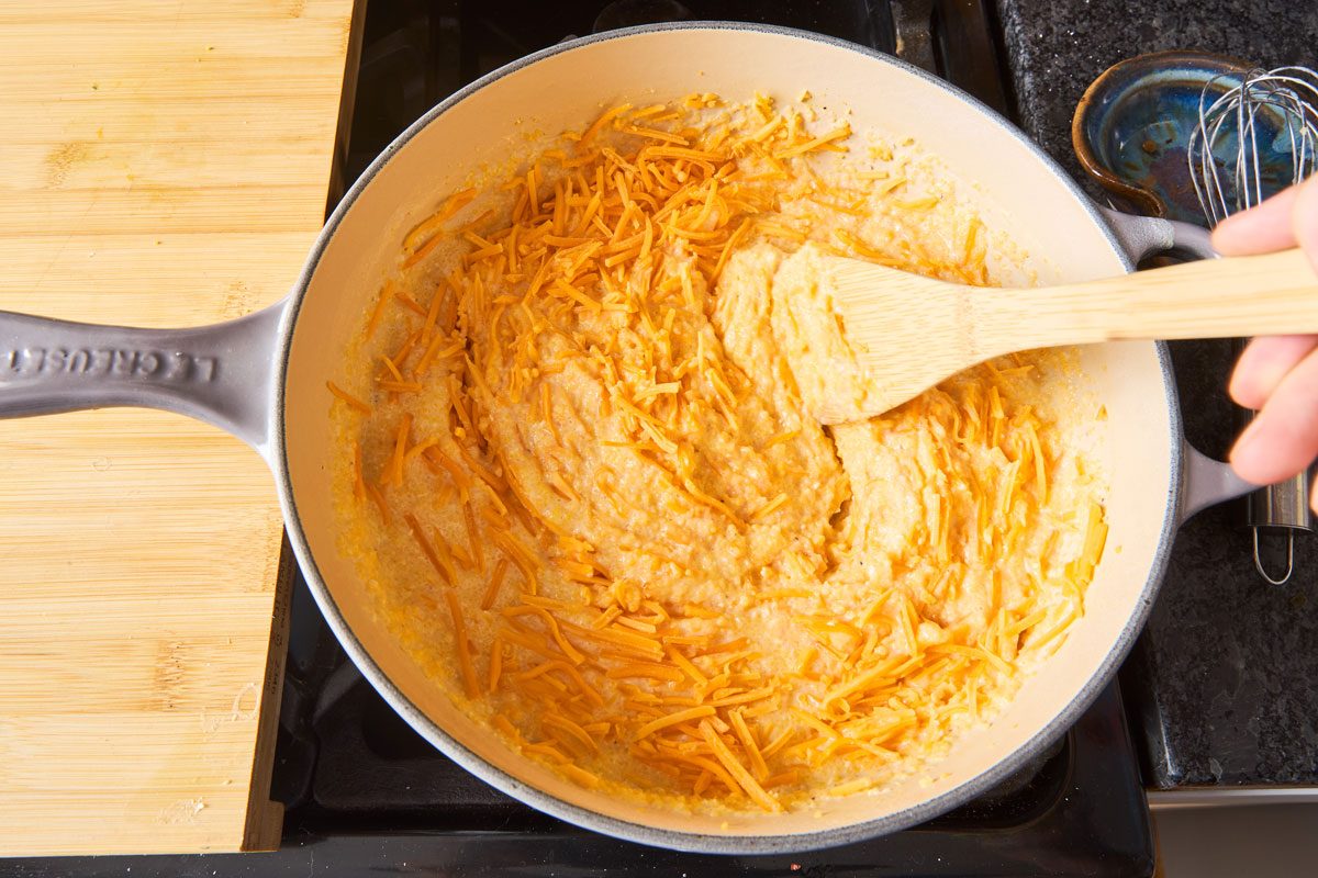 Shredded cheese being mixed into cooked grits on stovetop