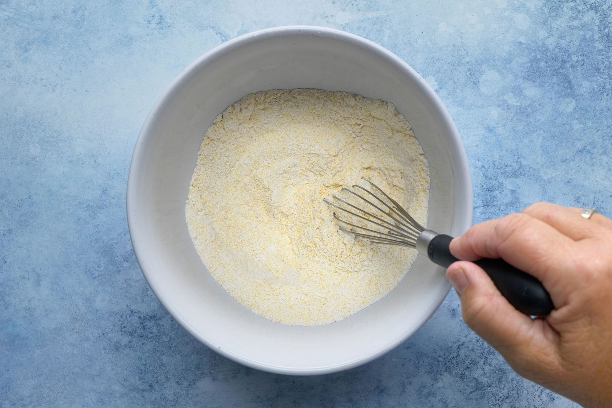 overhead shot; light blue background; In a medium bowl, combining flour, cornmeal, sugar, baking powder and salt;