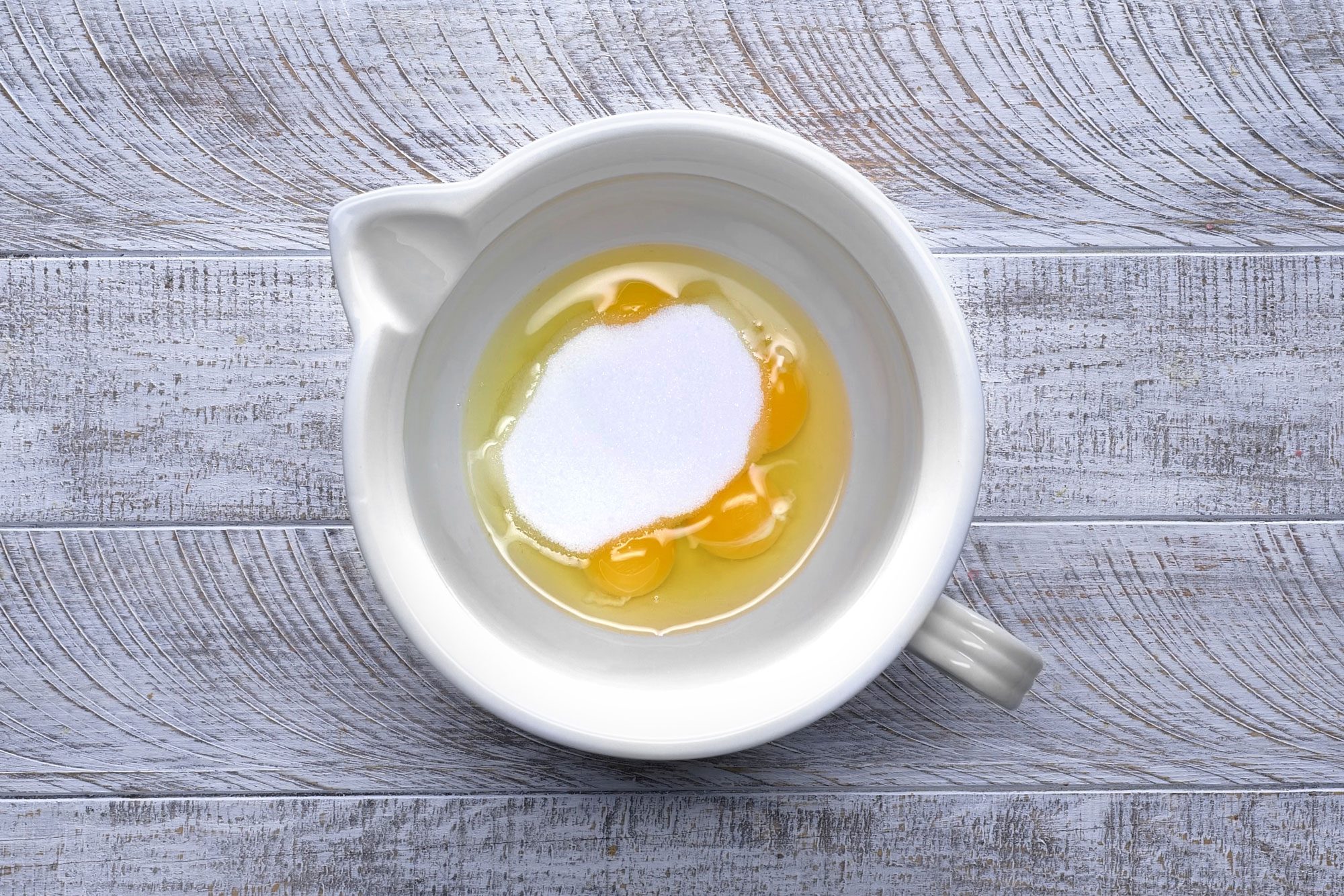 Overhead shot of a large bowl; whisk eggs; sugar and salt until blended but not foamy; wooden background;
