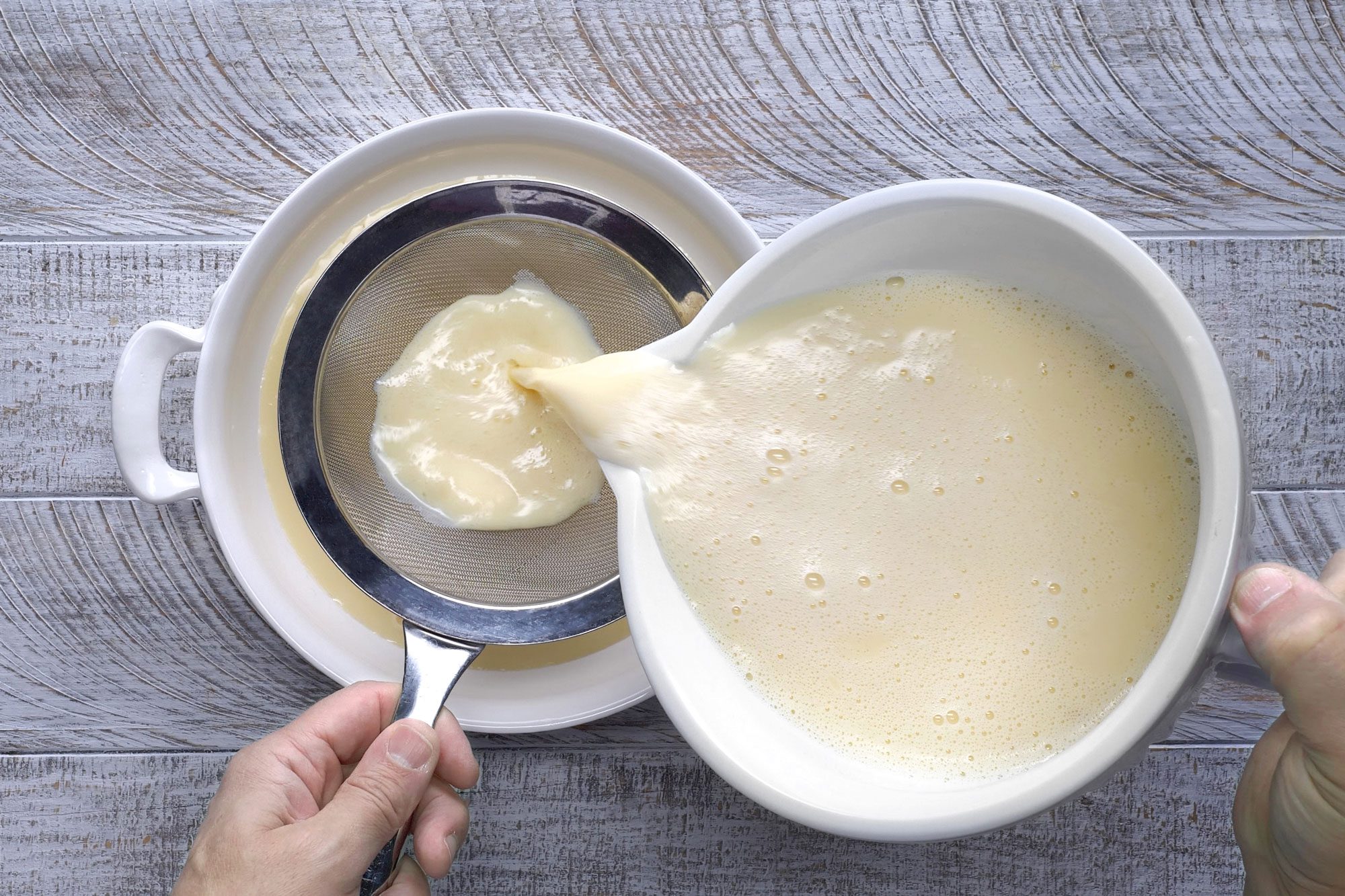 Overhead shot of pour egg mixture through a strainer into a round baking dish; wooden background;